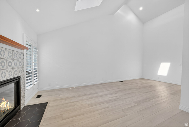 6969 South 855 East Midvale, UT 84047 - Photo 15 of 55 Vaulted ceiling room featuring a fireplace with patterned tile surround and wood mantel, white plantation shutters, skylight, recessed lighting, and light wood-finish flooring