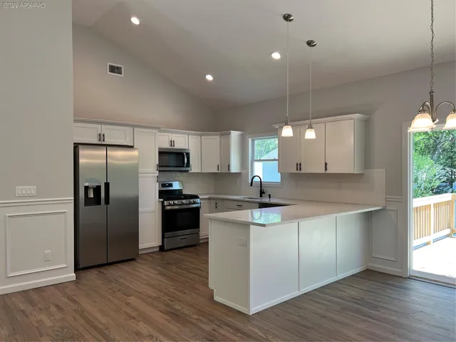 a large kitchen with stainless steel appliances a large counter top a sink a refrigerator and a window