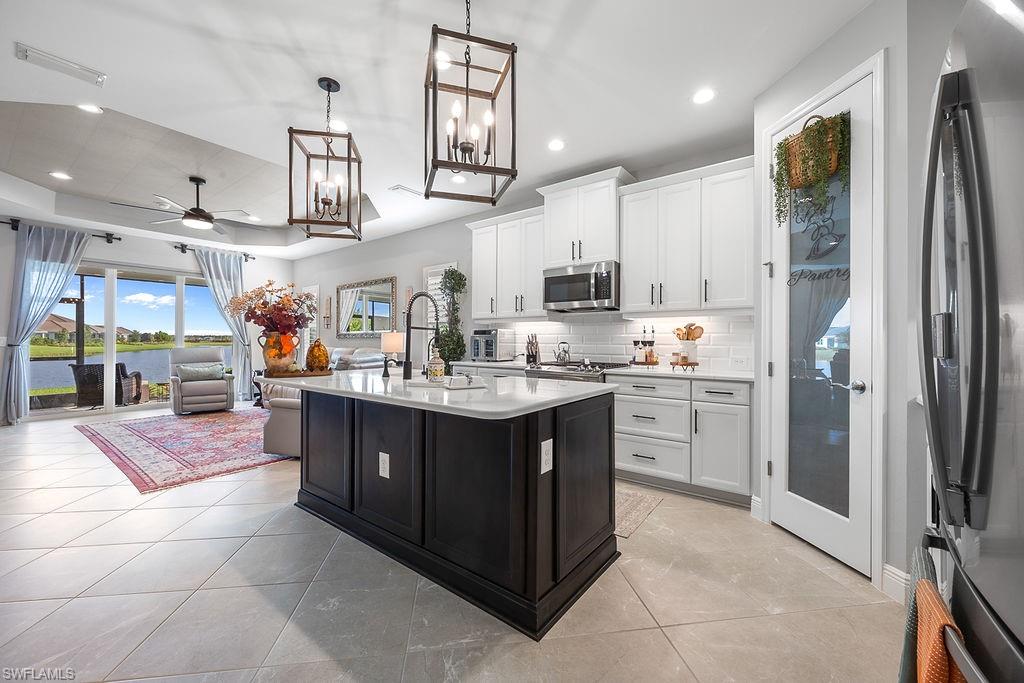 4584 Centaurus Circle Naples, FL 34120 - Photo 13 of 40 Kitchen featuring stainless steel appliances, white cabinets, a kitchen island with sink, backsplash, and a raised ceiling