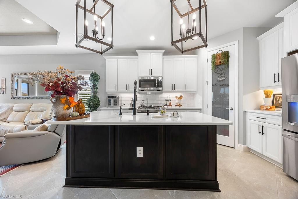 4584 Centaurus Circle Naples, FL 34120 - Photo 15 of 40 Kitchen with hanging light fixtures, decorative backsplash, white cabinets, stainless steel appliances, and a kitchen island with sink