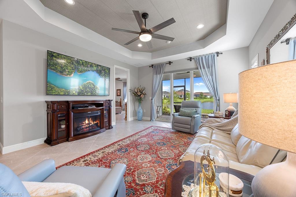 4584 Centaurus Circle Naples, FL 34120 - Photo 18 of 40 Living room featuring a tray ceiling, a glass covered fireplace, recessed lighting, and a ceiling fan