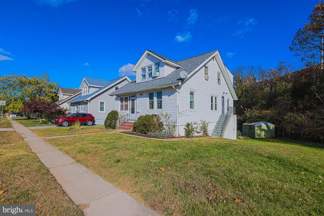 a view of a white house in front of a big yard with plants and large trees