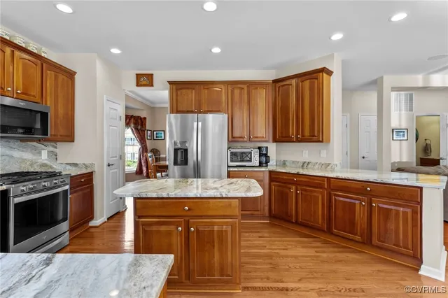 a kitchen with stainless steel appliances granite countertop a refrigerator a stove top oven a sink dishwasher and wooden cabinets with wooden floor
