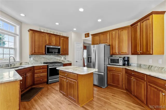 a kitchen with stainless steel appliances granite countertop a stove top oven a sink dishwasher and a refrigerator with wooden cabinets