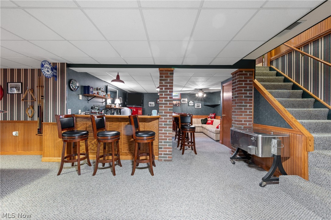 10400 Stoneacre Road Northwest Canal Fulton, OH 44614 - Photo 26 of 44 Indoor wet bar featuring carpet floors, a paneled ceiling, wooden walls, and stairs
