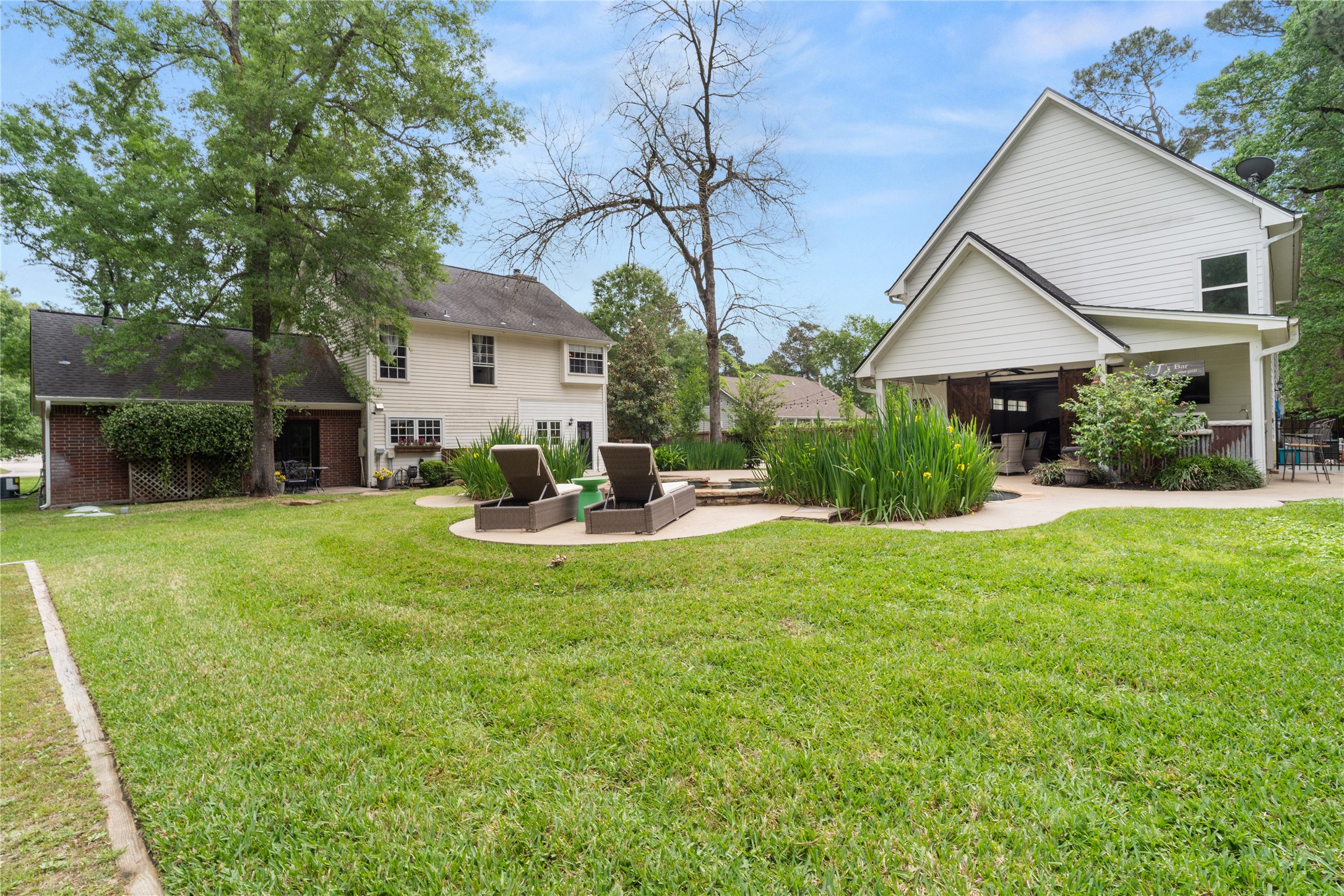 36 Wind River Drive Conroe, TX 77384 - Photo 17 of 45 This photo showcases a serene backyard with a pool surrounded by lush greenery and a spacious patio with seating. The area includes a cozy covered porch with ceiling fan, perfect for outdoor relaxation. The detached garage living space is to the right.