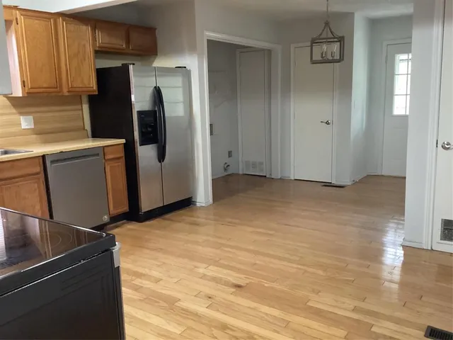 a view of a refrigerator in kitchen and an empty room with wooden floor