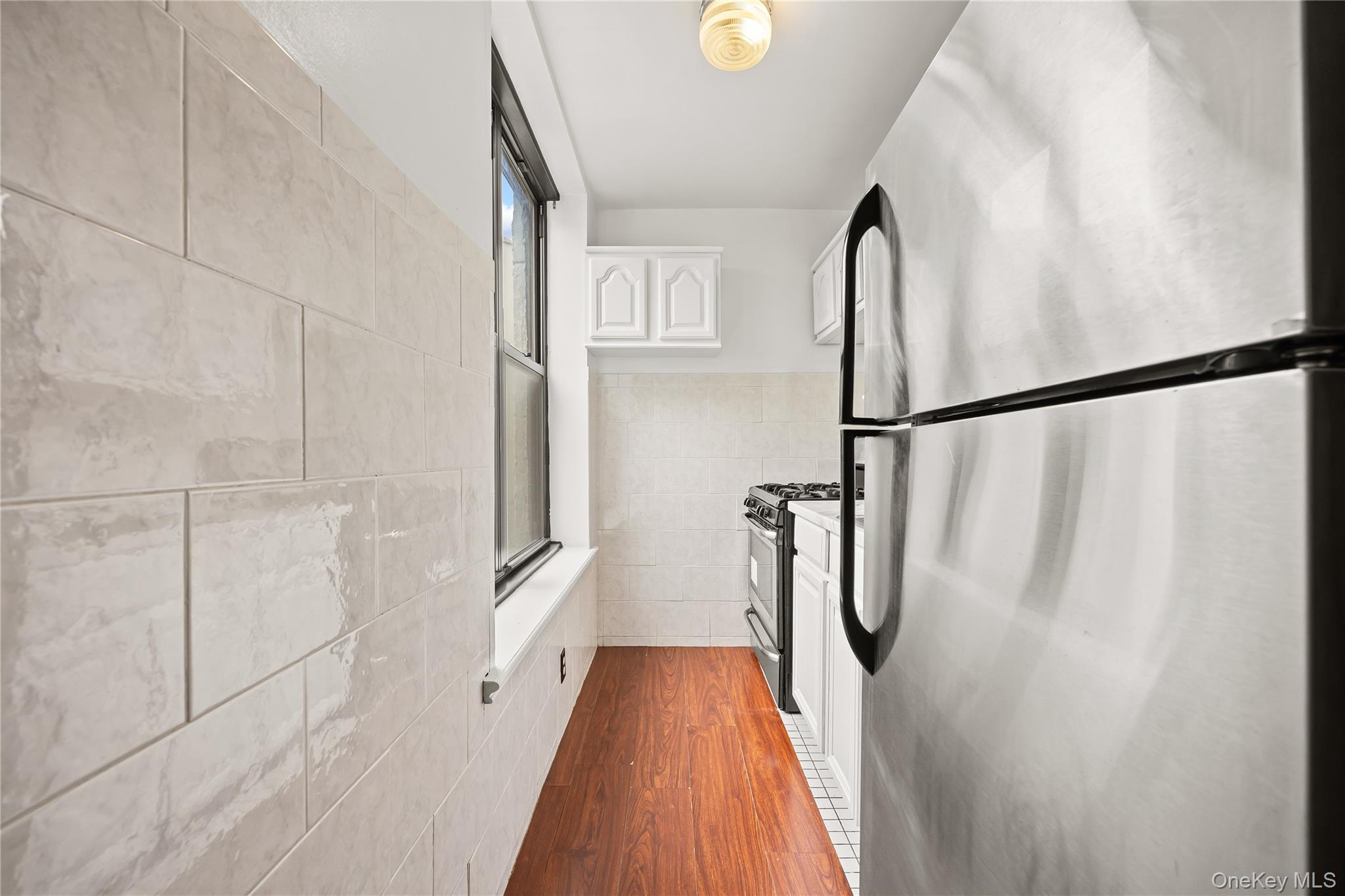 1423 31st Avenue, Unit 4E Queens, NY 11106 - Photo 11 of 23 Kitchen featuring stainless steel appliances, white cabinets, dark wood-type flooring, tile walls, and light countertops