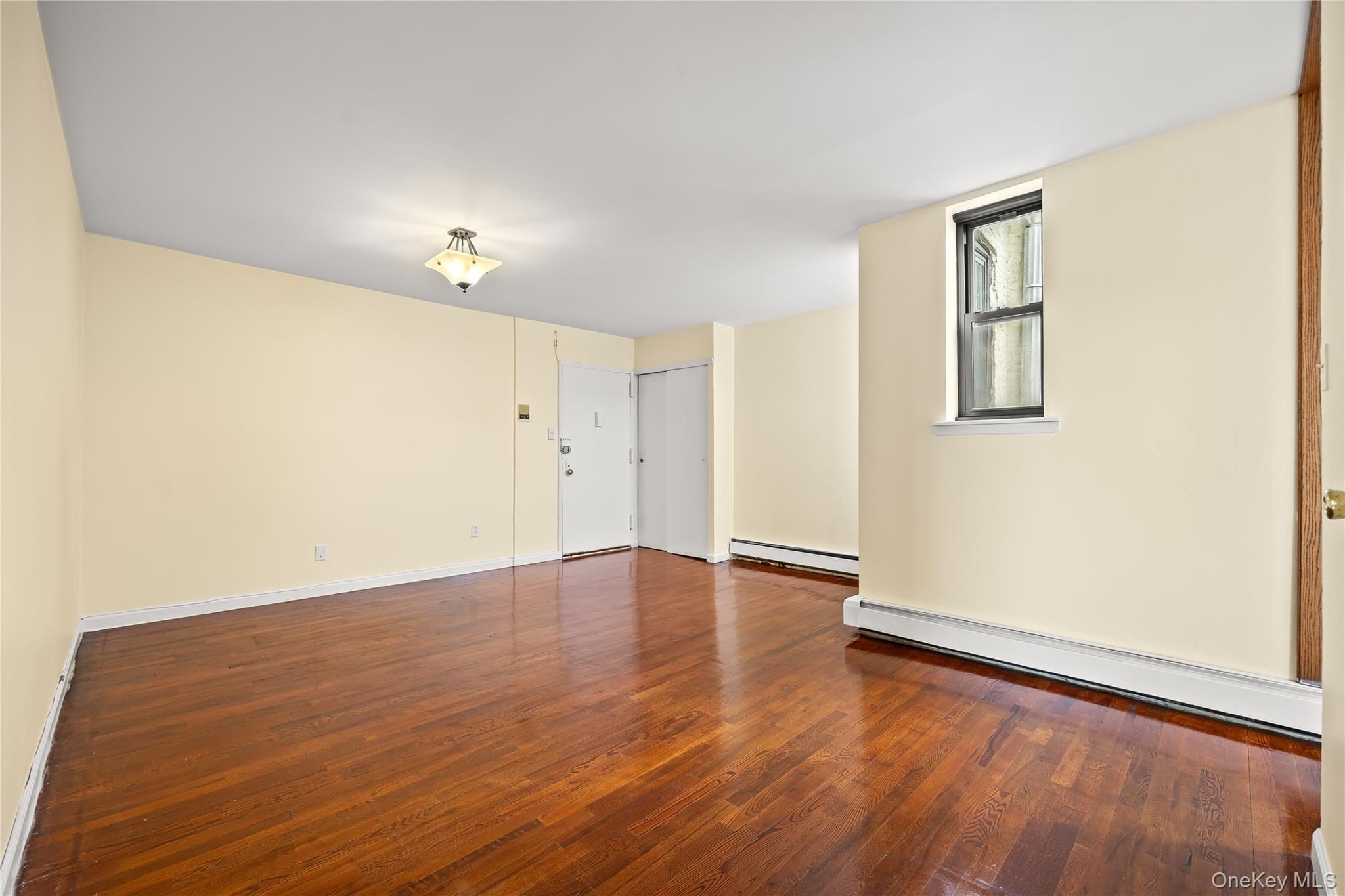 1423 31st Avenue, Unit 4E Queens, NY 11106 - Photo 6 of 23 Spare room with dark wood-style flooring and baseboard heating