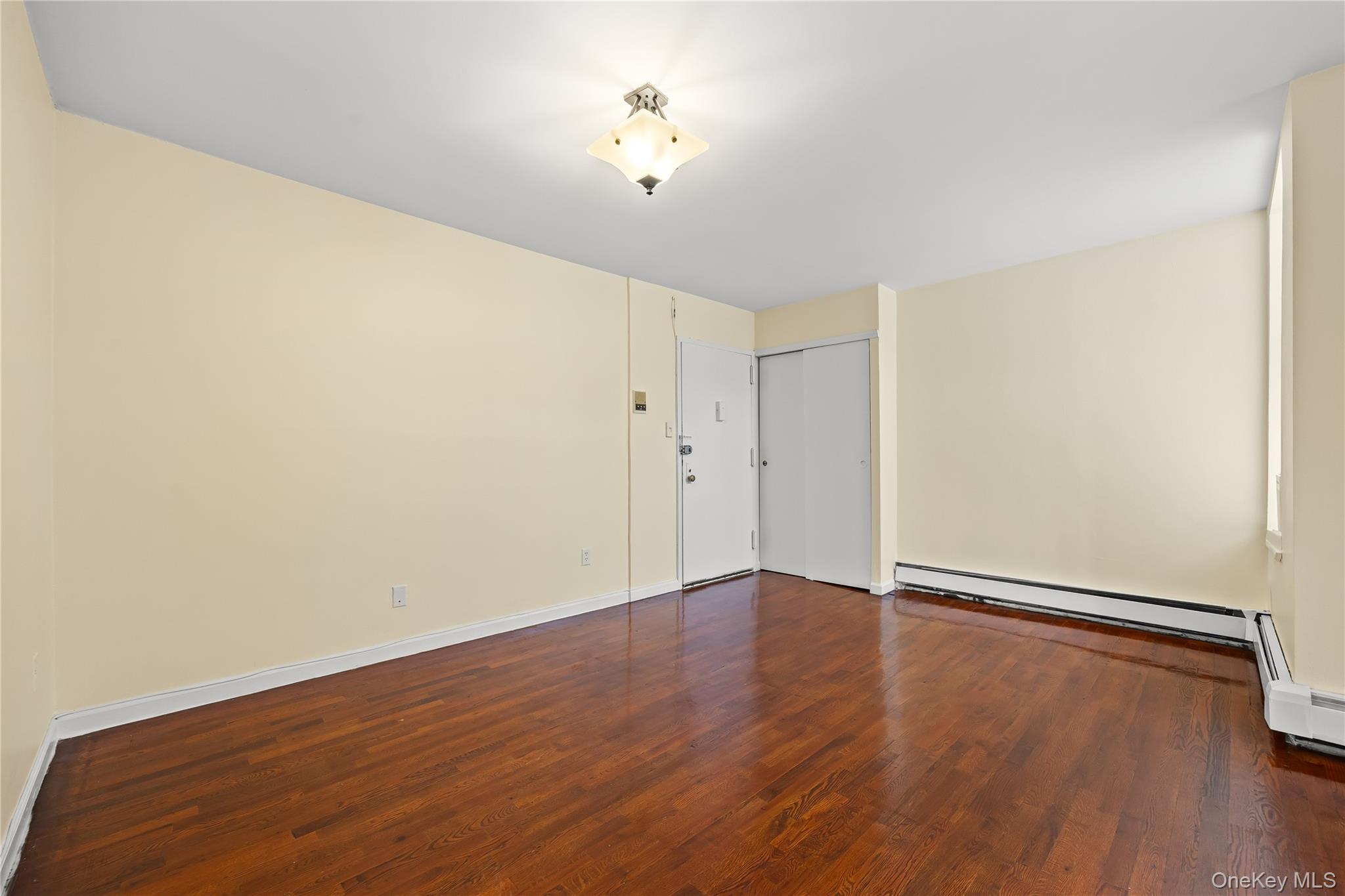 1423 31st Avenue, Unit 4E Queens, NY 11106 - Photo 7 of 23 Unfurnished room with dark wood-style flooring and a baseboard heating unit