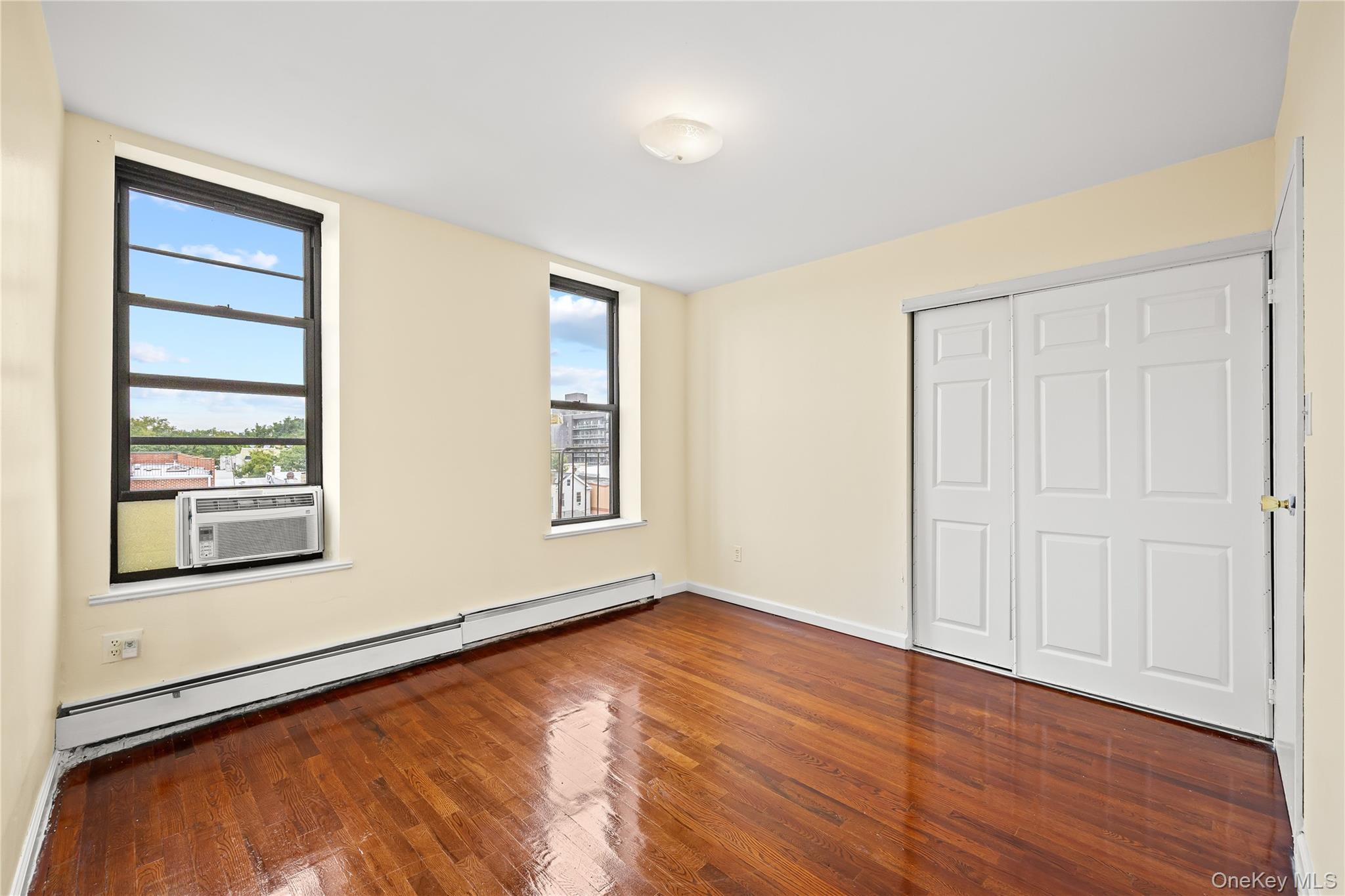 1423 31st Avenue, Unit 4E Queens, NY 11106 - Photo 8 of 23 Unfurnished bedroom with baseboard heating, dark wood finished floors, and a closet