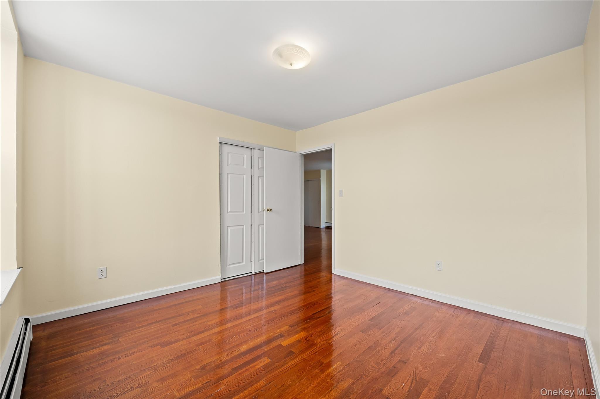 1423 31st Avenue, Unit 4E Queens, NY 11106 - Photo 10 of 23 Empty room with baseboard heating and wood finished floors