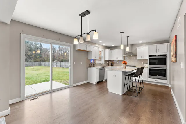 a open kitchen with stainless steel appliances granite countertop a stove top oven a refrigerator and a dining table with wooden floor