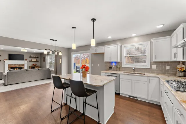 a kitchen with stainless steel appliances granite countertop a stove top oven a sink a refrigerator and white cabinets with wooden floor