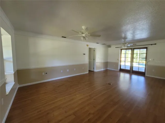 an empty room with wooden floor ceiling fan and window