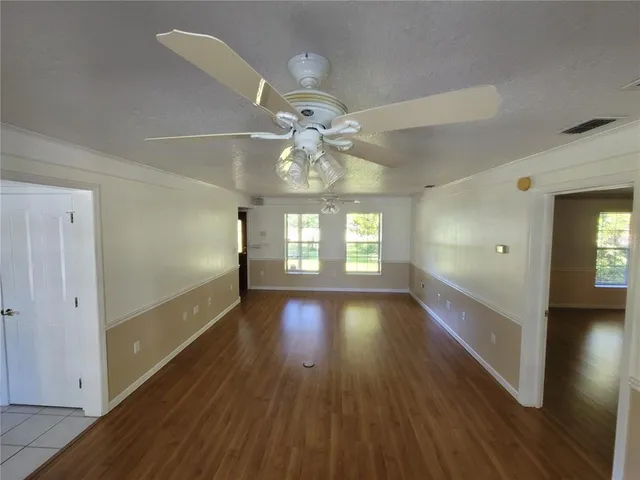 a view of an empty room with wooden floor and a fan
