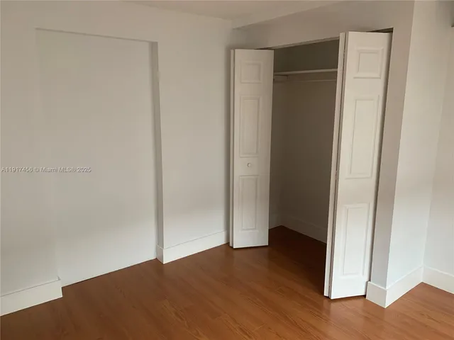 a view of an empty room with wooden floor and closet