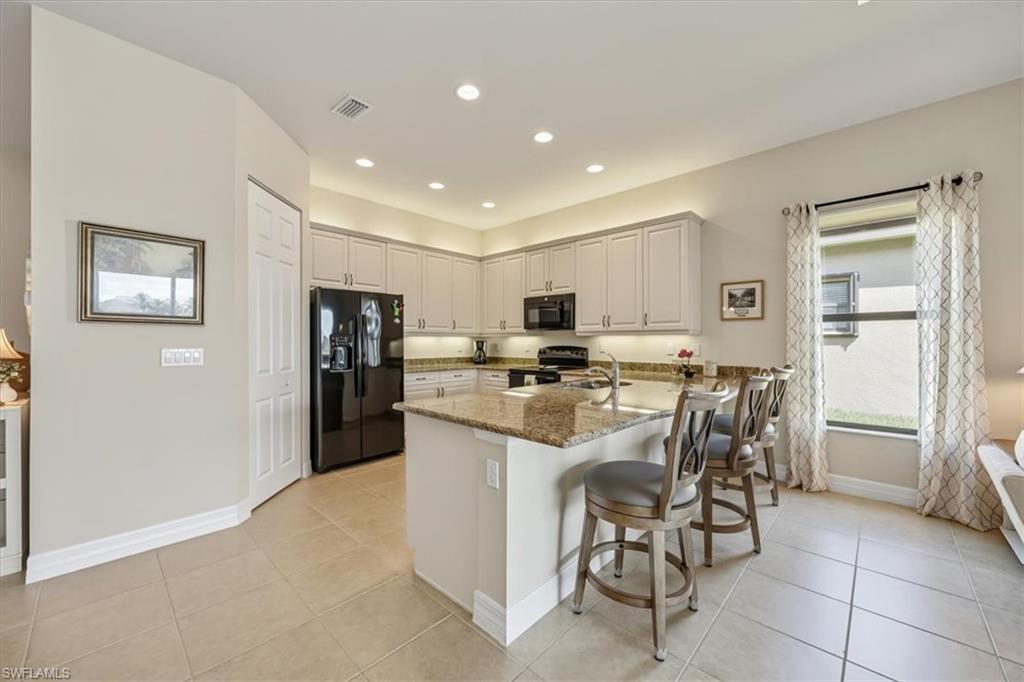 13466 Sumter Lane Naples, FL 34109 - Photo 9 of 36 Kitchen featuring black appliances, light stone counters, a kitchen bar, light tile patterned floors, and recessed lighting