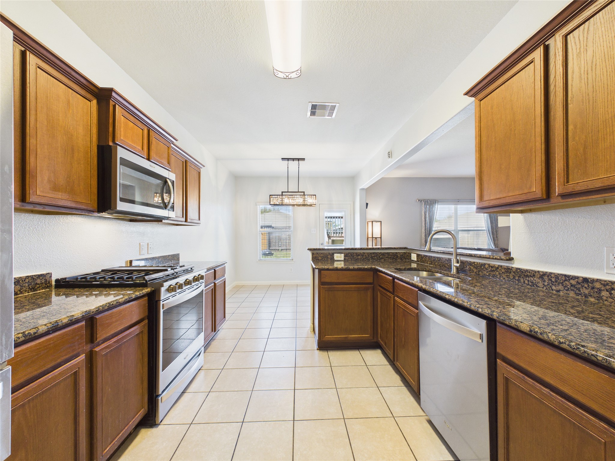 911 Marigold Road Baytown, TX 77521 - Photo 15 of 32 This kitchen features wood cabinetry, granite countertops, and stainless steel appliances. An open layout connects to a dining area, enhancing the space's functionality and flow.