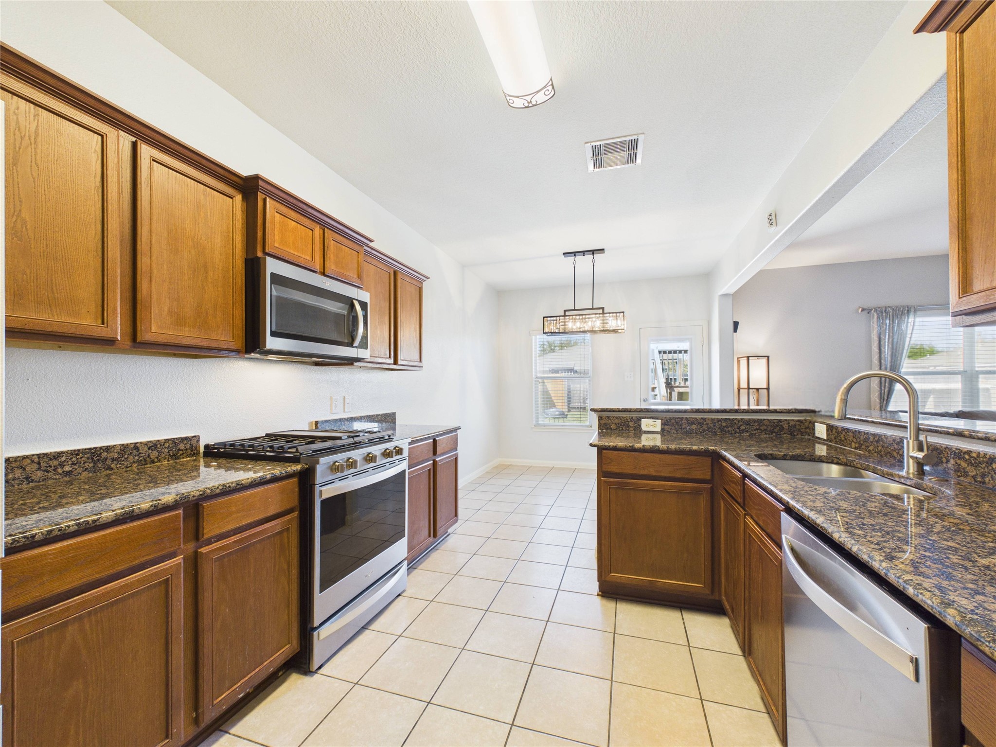 911 Marigold Road Baytown, TX 77521 - Photo 16 of 32 This kitchen features granite countertops, wooden cabinetry, a gas touchscreen stove, and stainless steel appliances.