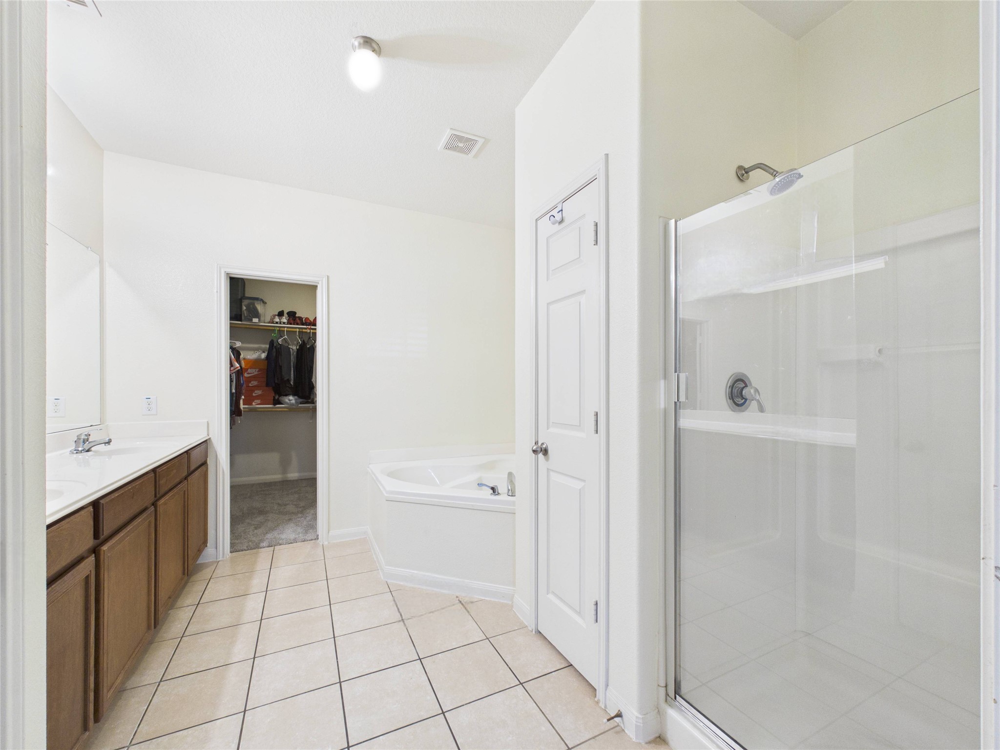 911 Marigold Road Baytown, TX 77521 - Photo 7 of 32 This bathroom features a spacious layout with a glass-enclosed shower, a separate bathtub, double sinks and access to a walk-in closet. The neutral tile flooring and bright lighting create a clean, inviting atmosphere.