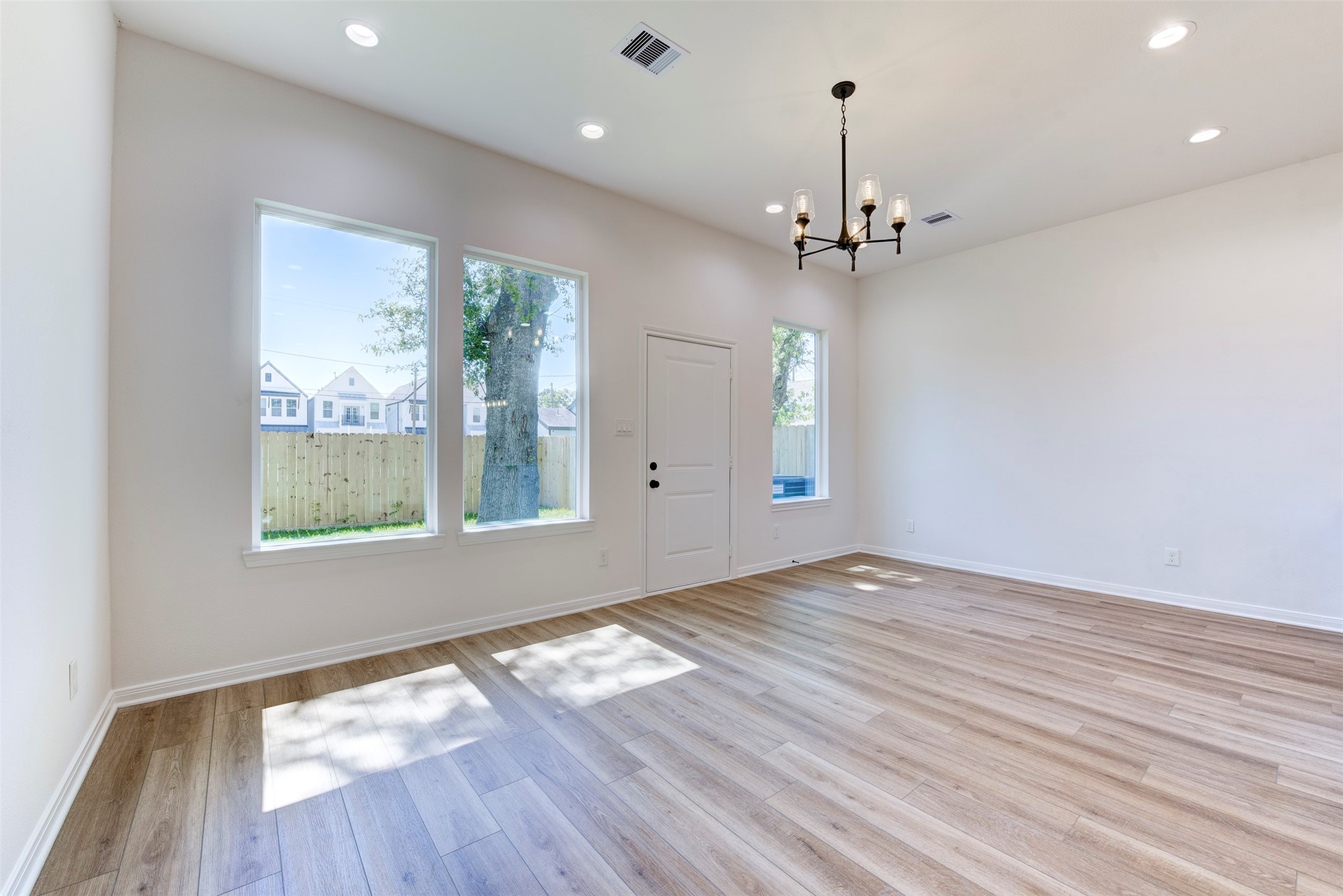 6807 Paris Street Houston, TX 77021 - Photo 15 of 37 Living area framed by large windows that bring in natural light, paired with wood-look LVP flooring and tall ceilings. Statement chandelier adds a refined focal point, while direct access to the backyard enhances everyday flow.