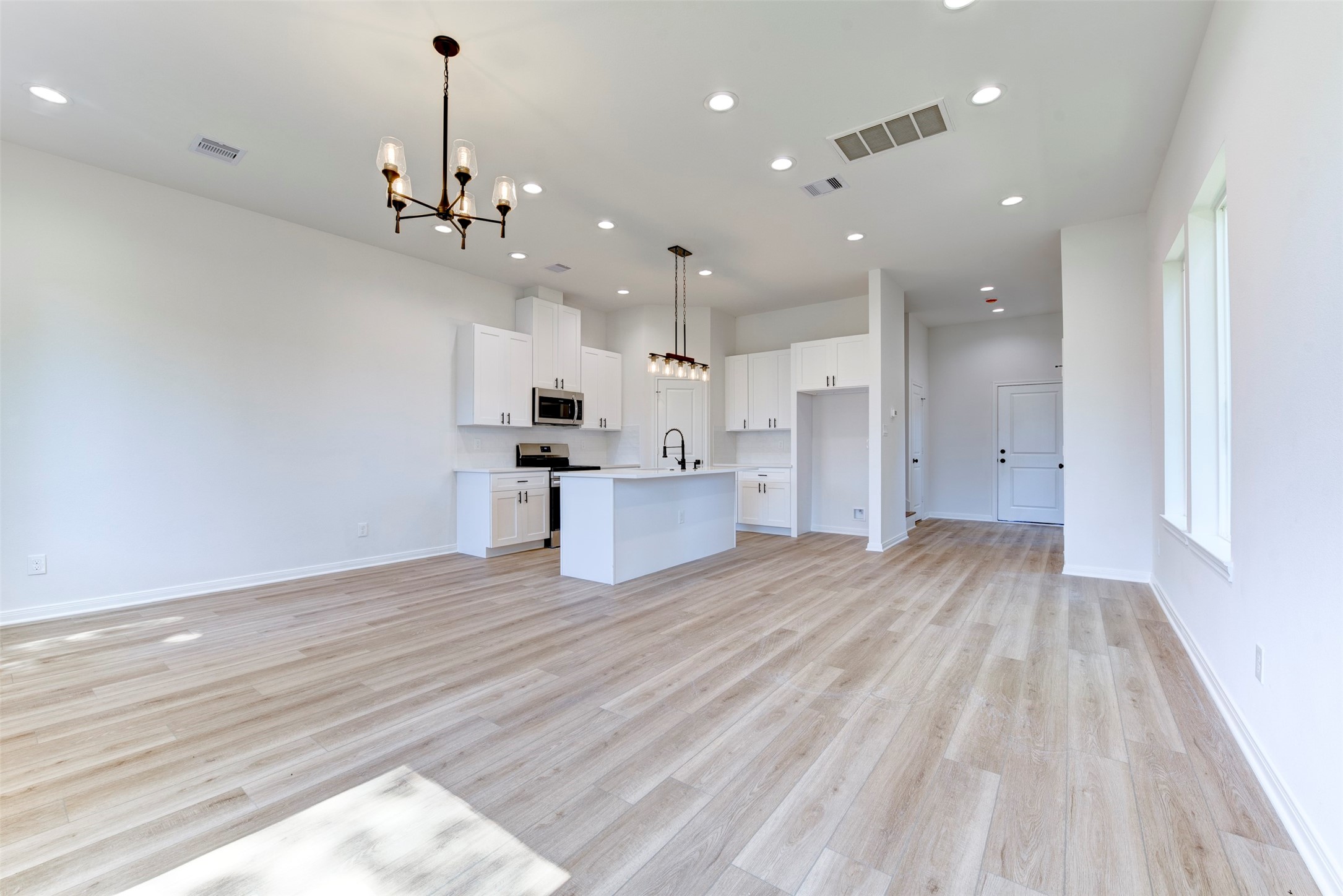 6807 Paris Street Houston, TX 77021 - Photo 16 of 37 Expansive open-concept layout with wood-look LVP flooring, tall ceilings, and abundant recessed lighting throughout. Seamless flow from living to kitchen, anchored by a central island and complemented by clean white cabinetry and modern fixtures.