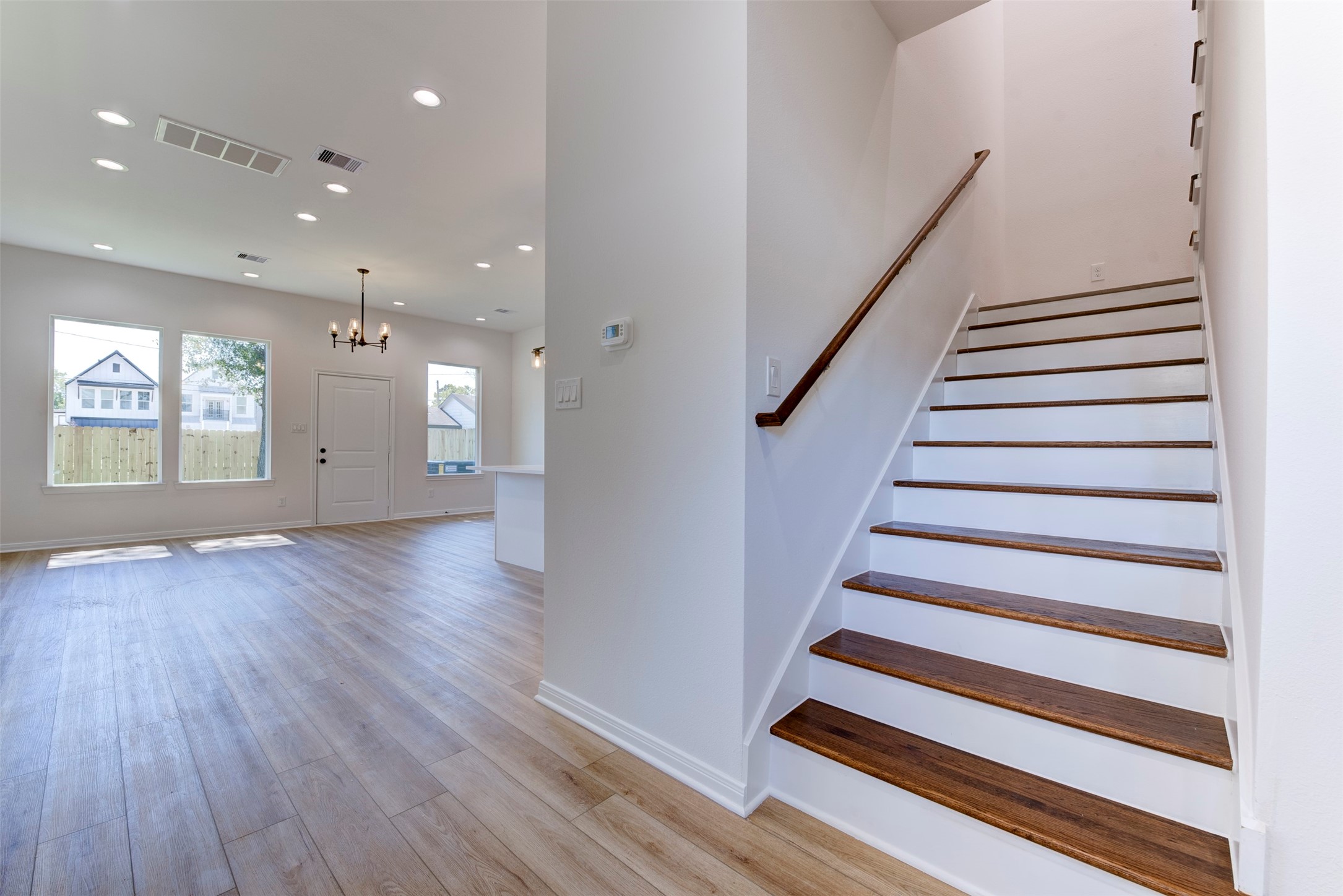 6807 Paris Street Houston, TX 77021 - Photo 4 of 37 Seamless transition into the open-concept living space highlighted by wood-look LVP flooring, tall ceilings, and abundant natural light. Recessed lighting is thoughtfully layered throughout. Staircase features warm wood treads with crisp white risers and a clean handrail, adding a refined contrast to the home’s bright, neutral palette.