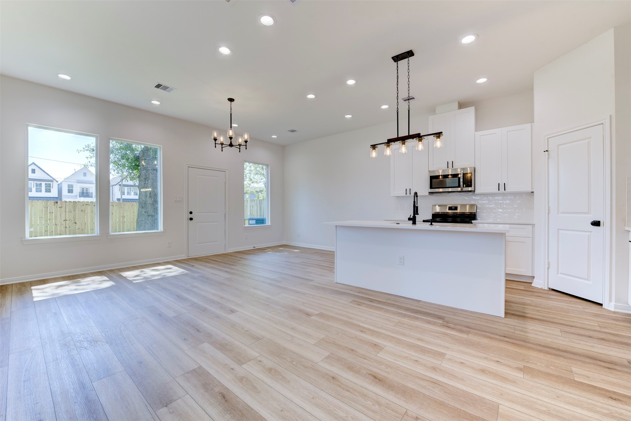 6807 Paris Street Houston, TX 77021 - Photo 8 of 37 Open-concept living filled with natural light, featuring wood-look LVP flooring, tall ceilings, and a seamless flow between living, dining, and kitchen. Recessed lighting and statement fixtures add warmth, creating a bright and inviting everyday space.