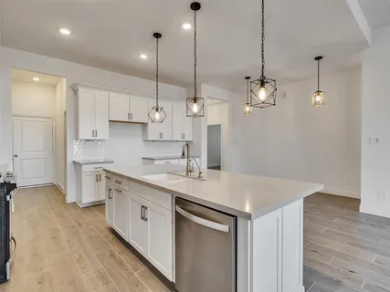 a kitchen with a sink dishwasher and white cabinets with wooden floor