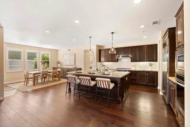 a large kitchen with stainless steel appliances kitchen island granite countertop a stove a sink a refrigerator and a dining table with wooden floor