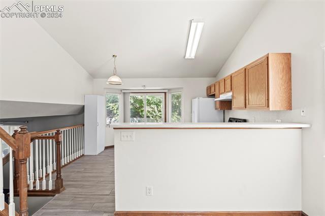 4763 Brant Road Colorado Springs, CO 80911 - Photo 8 of 26 Kitchen featuring pendant lighting, white refrigerator, light hardwood / wood-style flooring, vaulted ceiling, and kitchen peninsula