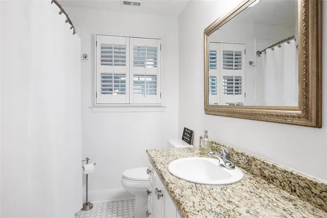 a bathroom with a granite countertop sink toilet a mirror and a window
