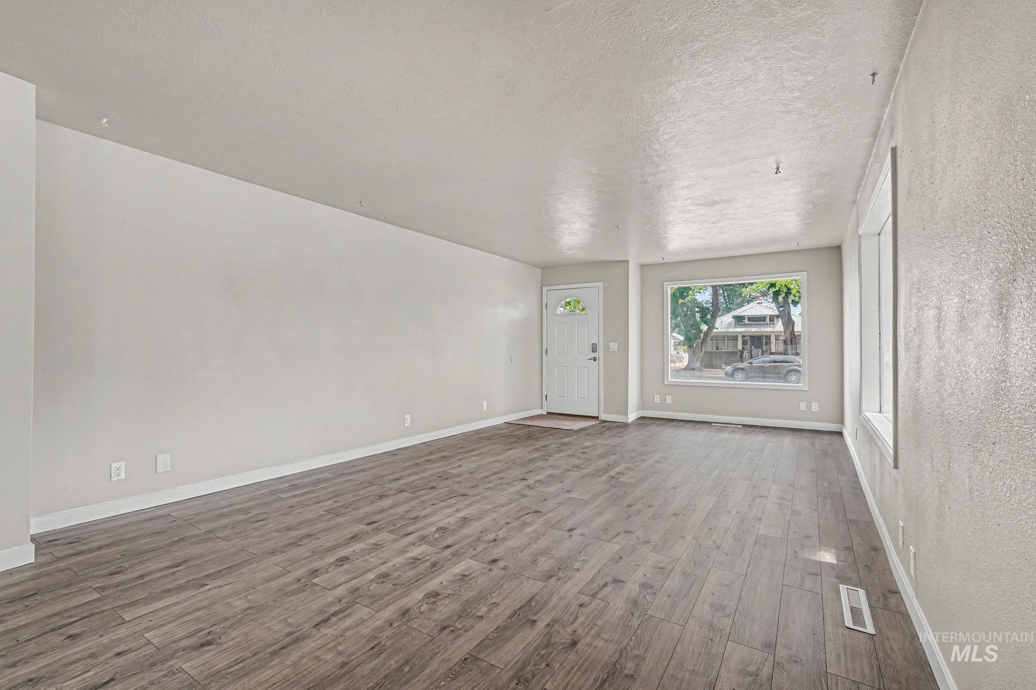 1023 State Street Weiser, ID 83672 - Photo 4 of 25 Spacious living area featuring wood-finish flooring, light grey wall paint, white baseboards, and a prominent front-facing window