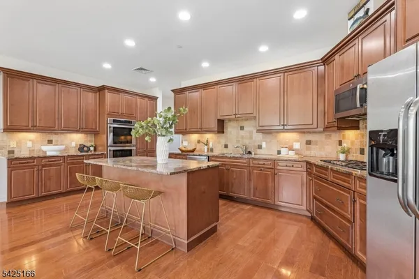 a kitchen with stainless steel appliances granite countertop a stove top oven a sink dishwasher and a refrigerator with wooden floor