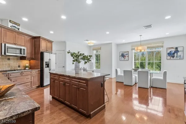 a kitchen with stainless steel appliances granite countertop a refrigerator a stove top oven and a dining table with wooden floor