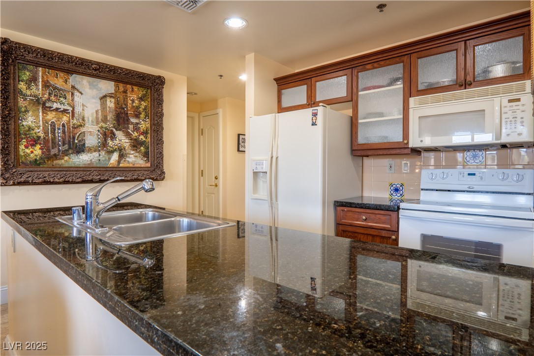 30 Strada Di Villaggio, Unit 617 Henderson, NV 89011 - Photo 9 of 34 Kitchen featuring white appliances, decorative backsplash, glass insert cabinets, recessed lighting, and dark stone counters