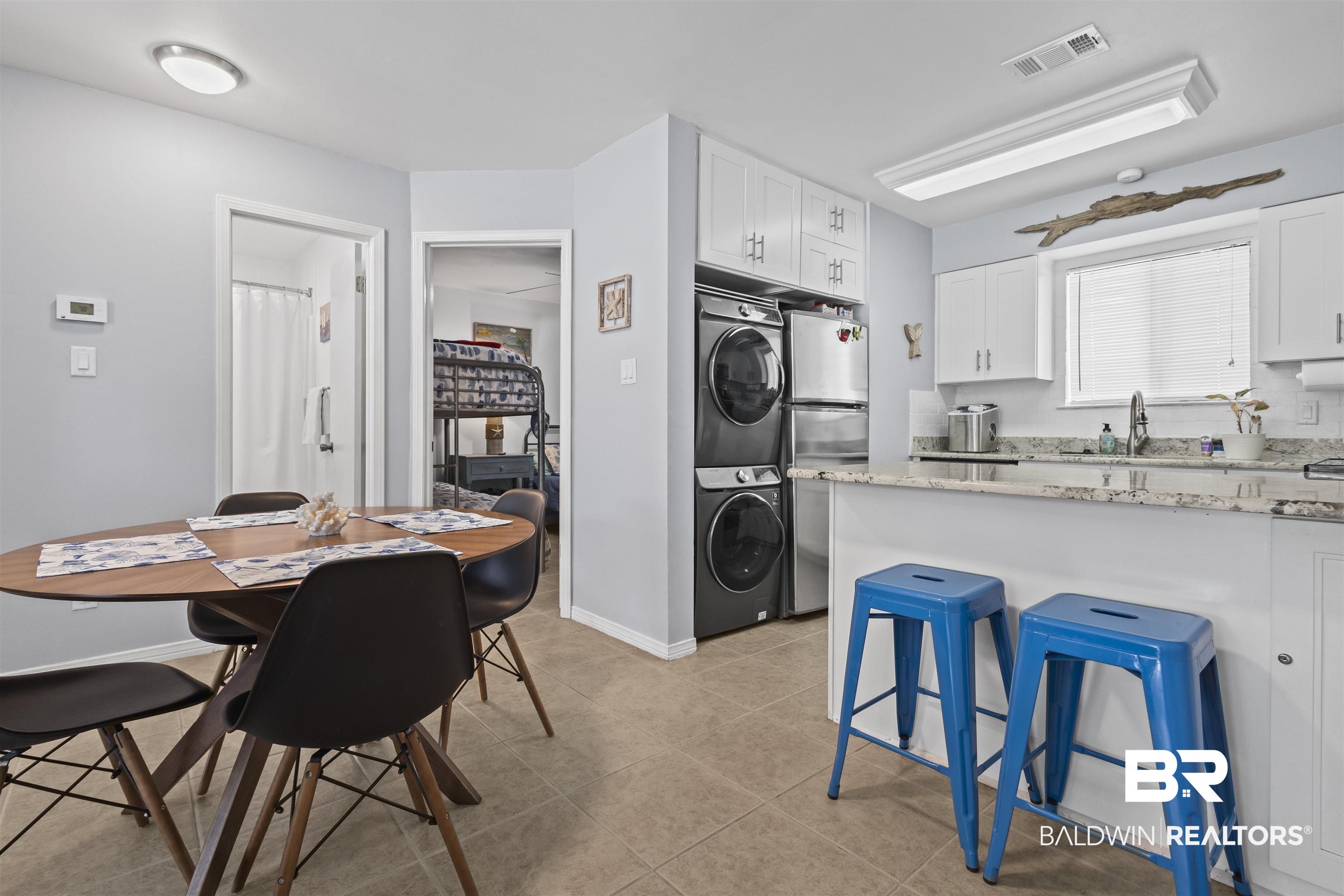 25925 Canal Road, Unit 207 Orange Beach, AL 36561 - Photo 16 of 42 Kitchen featuring a kitchen breakfast bar, light stone counters, white cabinetry, and light tile floors