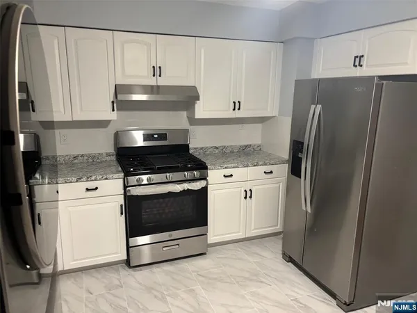 a kitchen with granite countertop a refrigerator stove and white cabinets