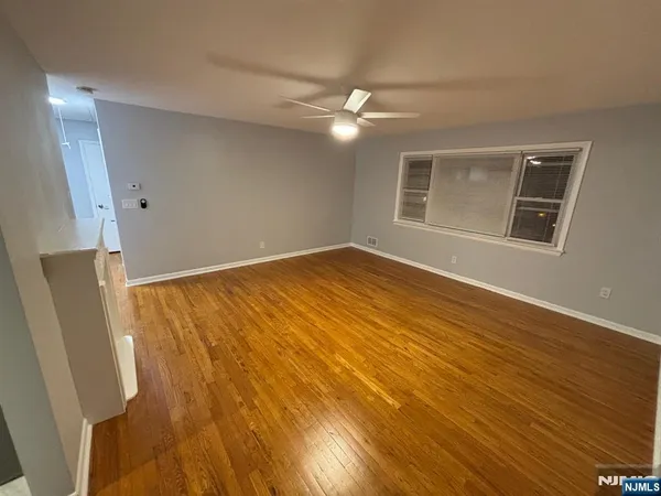 a view of an empty room with wooden floor and a ceiling fan