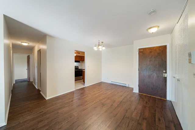 a view of an empty room with wooden floor and a kitchen