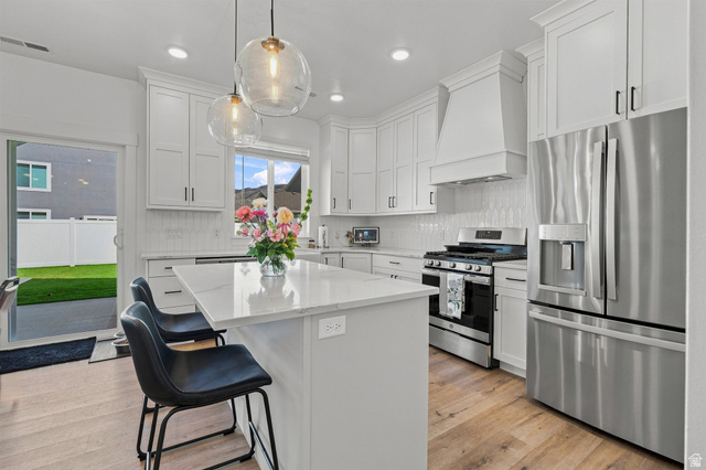 355 West 3085 South Logan, UT 84321 - Photo 10 of 40 White shaker cabinetry, stainless steel appliances, central island with seating, pendant lighting, and wood-finish flooring