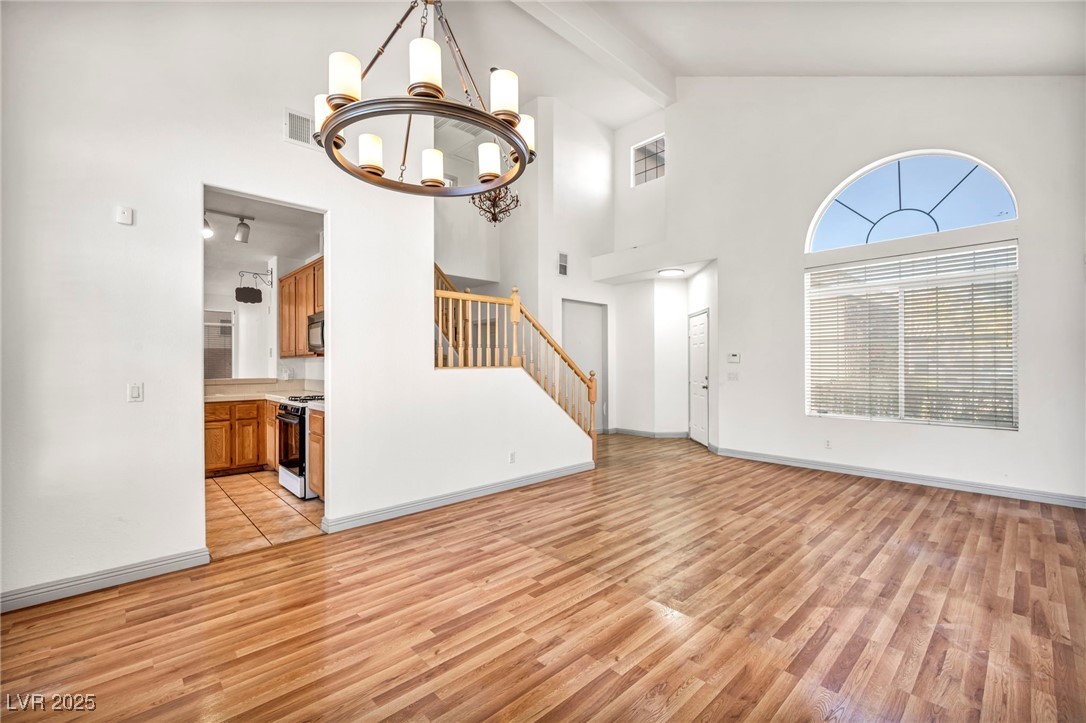 1704 Jack Rabbit Way Las Vegas, NV 89128 - Photo 11 of 25 Unfurnished living room with beamed ceiling, light wood finished floors, stairs, high vaulted ceiling, and a chandelier