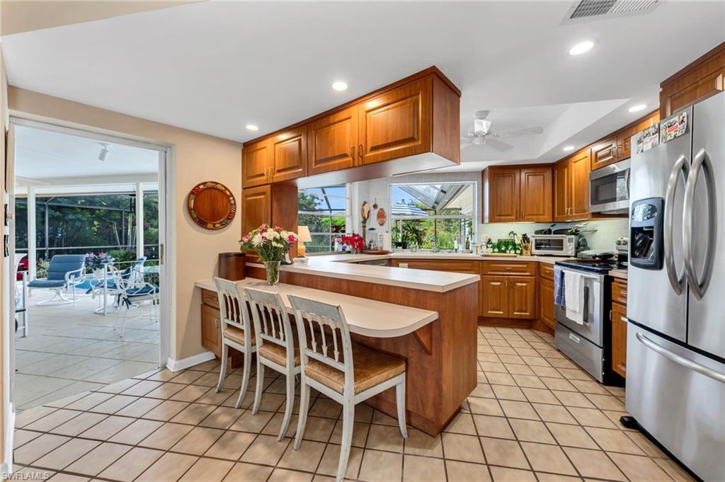 737 Anchor Rode Drive Naples, FL 34103 - Photo 8 of 21 Kitchen with a breakfast bar, light countertops, appliances with stainless steel finishes, brown cabinets, and a peninsula