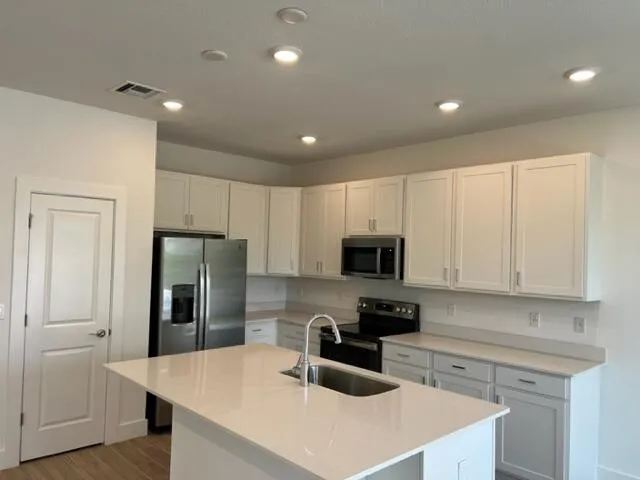 a kitchen with refrigerator a stove a sink and white cabinets