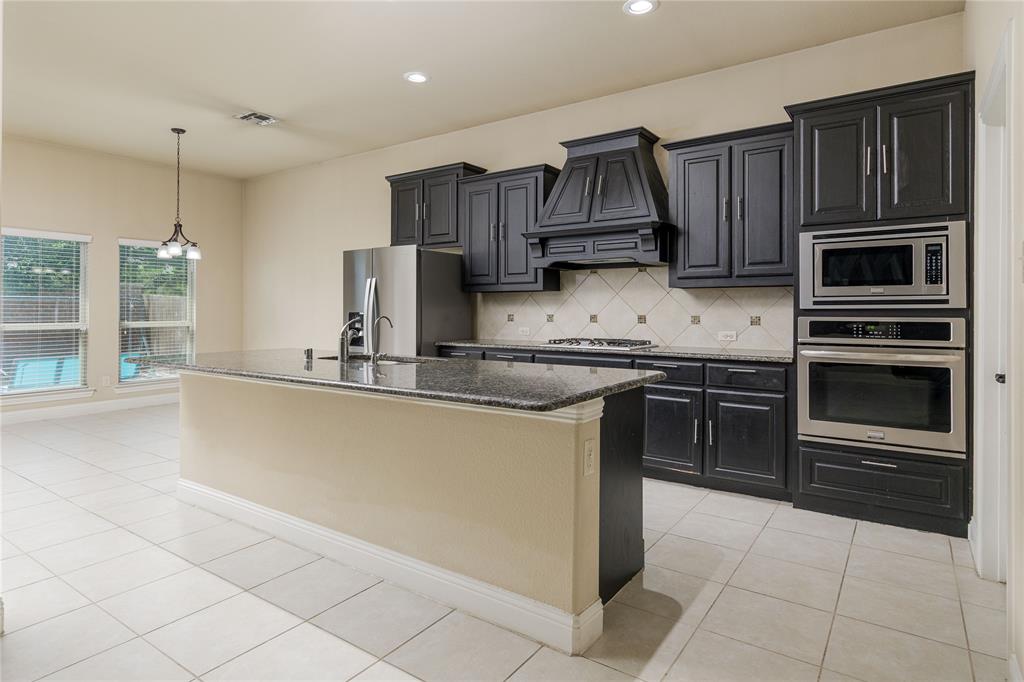 404 Tanner Square McKinney, TX 75072 - Photo 10 of 34 Kitchen featuring appliances with stainless steel finishes, premium range hood, a kitchen island with sink, tasteful backsplash, and light tile patterned floors