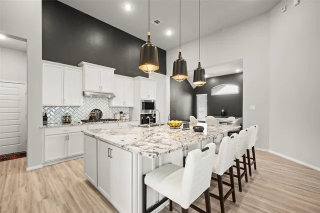 a kitchen with stainless steel appliances kitchen island granite countertop a stove a sink a refrigerator and white cabinets with wooden floor