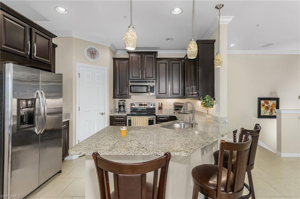 23550 Alamanda Drive, Unit 202 Estero, FL 34135 - Photo 13 of 26 a kitchen with granite countertop a table chairs microwave and cabinets