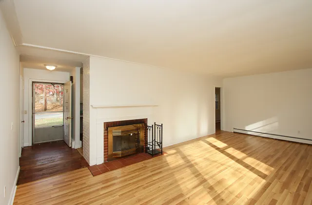 an empty room with wooden floor fireplace and windows