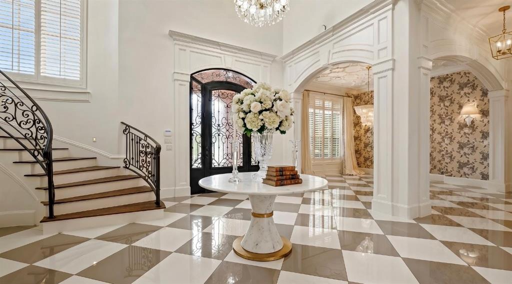 6900 Rockingham Court Colleyville, TX 76034 - Photo 7 of 40 Grand foyer featuring a checkerboard-patterned floor, an ornate wrought iron staircase, a decorative arched entryway, a substantial arched front door with glass and ironwork, and intricate wall paneling. Ai staged.